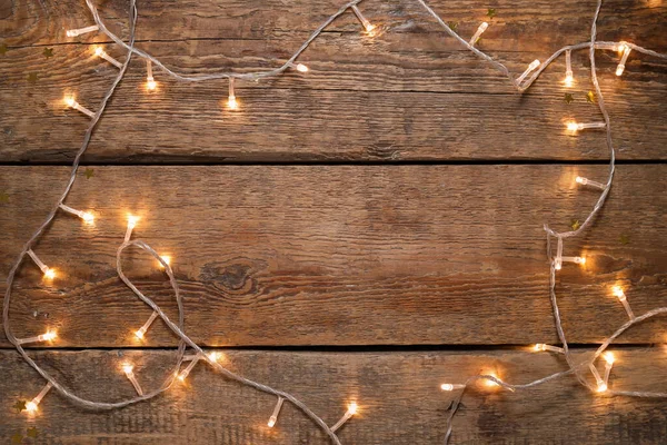 Ahşap arka planda parlayan Noel ışıklarından yapılmış çerçeve