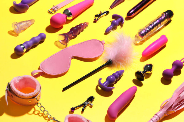 Различные секс-игрушки на жёлтом фоне, крупный план