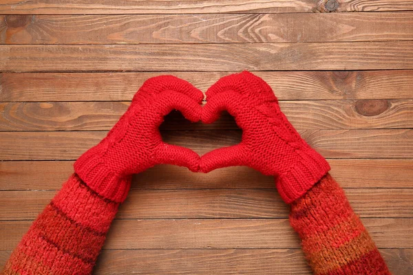 Woman in warm gloves making heart shape with her hands on wooden background, closeup