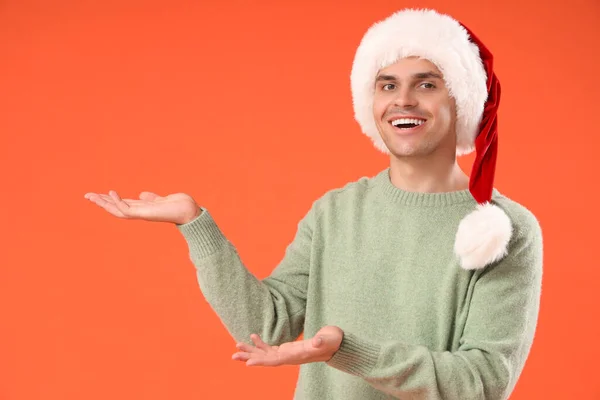 Glücklicher Junger Mann Mit Weihnachtsmütze Zeigt Auf Etwas Auf Orangefarbenem — Stockfoto