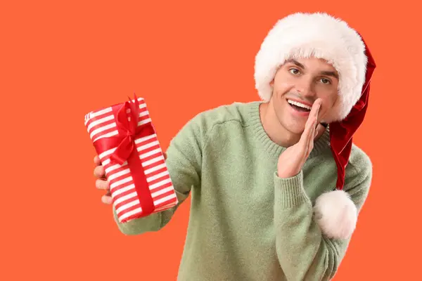 戴着圣诞礼帽 头戴橙色背景礼品盒的快乐年轻人 — 图库照片