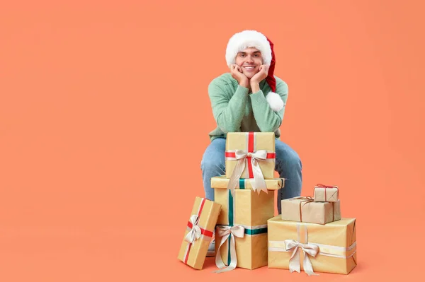 戴着圣诞礼帽 头戴礼品盒的快乐年轻人坐在椅子上 背对着橙色背景 — 图库照片