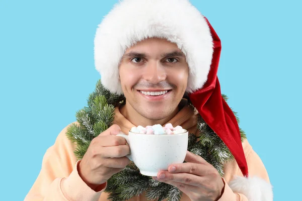 Šťastný Mladý Muž Santa Klobouk Vánoční Věnec Šálek Kakaa Modrém — Stock fotografie