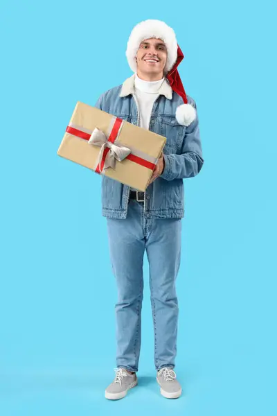 戴着圣诞礼帽 蓝底礼品盒的快乐年轻人 — 图库照片