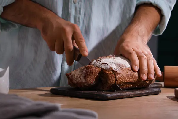 Genç adam fırında taze ekmek kesiyor.