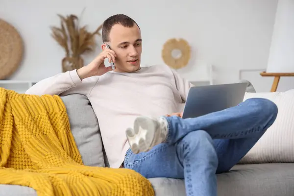 Bilgisayarlı Genç Adam Evdeki Koltukta Cep Telefonuyla Konuşuyor — Stok fotoğraf