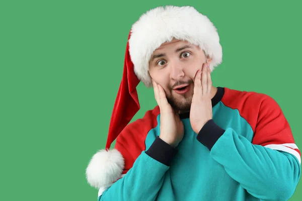 Schockierter Junger Mann Mit Weihnachtsmütze Auf Grünem Hintergrund — Stockfoto
