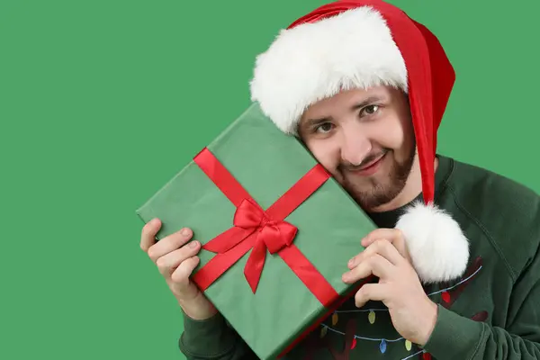 头戴圣诞礼帽 头戴绿色背景礼品盒的年轻人 — 图库照片