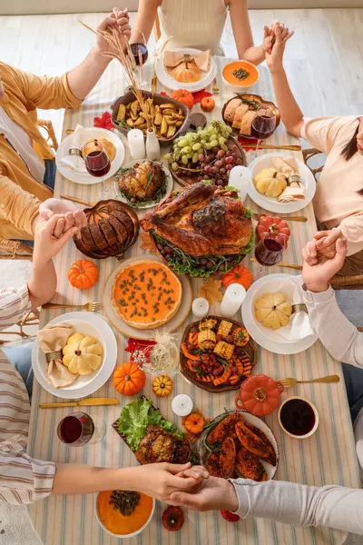 Group of young friends praying before dinner at festive table on Thanksgiving Day, top view