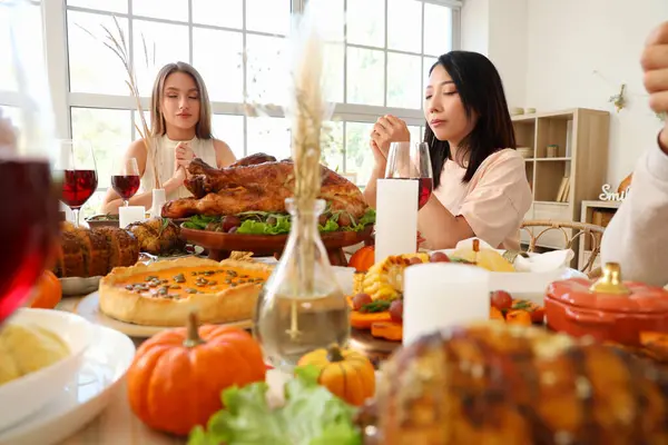 Group of young friends praying before dinner at festive table on Thanksgiving Day