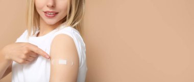 Kolunda yara bandı olan genç bir kadın bej arka planda ve mesaj için yeri var. Aşılama kavramı