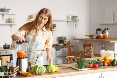 Genç bir kadın mutfakta blender ile sağlıklı smoothie yapıyor.