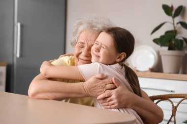 Küçük kız ve büyükannesi mutfakta sarılıyorlar.