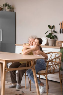 Küçük kız ve büyükannesi mutfakta sarılıyorlar.