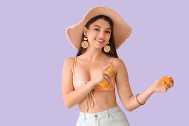 Leylak arka planına güneş kremi süren genç bir kadın.