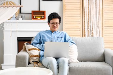 Genç Asyalı adam izin gününde dizüstü bilgisayar kullanıyor.