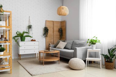 Gri kanepe, ahşap sehpa ve ev bitkileriyle aydınlık oturma odasının içinde.