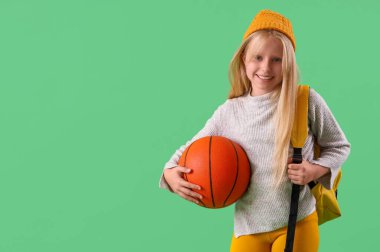 Yeşil arka planda top ve sırt çantalı küçük kız.