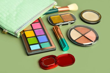 Yeşil arka planda farklı dekoratif kozmetik ürünlere sahip çanta