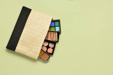 Yeşil arka planda farklı dekoratif kozmetik ürünlere sahip hasır çanta.