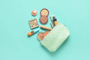 Turkuaz arka planda farklı dekoratif kozmetik ürünlere sahip çanta
