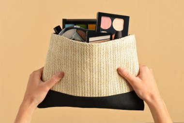 Sarı arka planda dekoratif kozmetik ürünleri olan bir çanta tutan kadın.