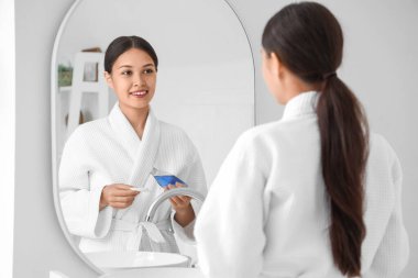 Banyoda aynanın yanında bir şişe mikiler suyu ve pamuk yastıklı genç Asyalı kadın.