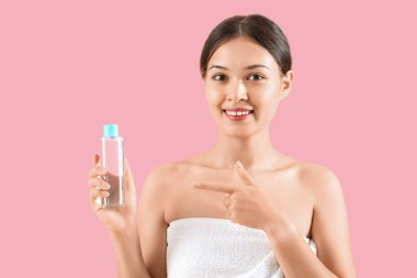 Genç Asyalı bir kadın pembe arka planda su şişesini işaret ediyor. Yakın plan.