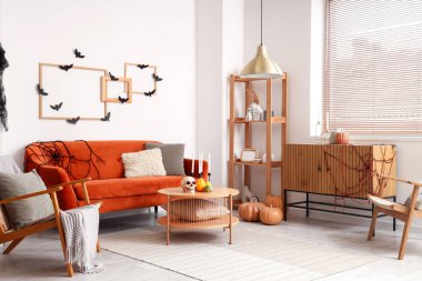 Cadılar Bayramı için dekore edilmiş oturma odasının içinde kırmızı kanepe ve koltuklar var.