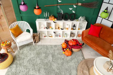 Cadılar Bayramı için dekore edilmiş oturma odasının içinde kırmızı kanepe ve raf ünitesi var.