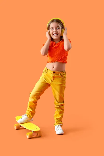 Nettes Kleines Mädchen Mit Kopfhörer Und Skateboard Auf Orangefarbenem Hintergrund — Stockfoto