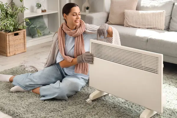 stock image Young woman with plaid warming near radiator at home