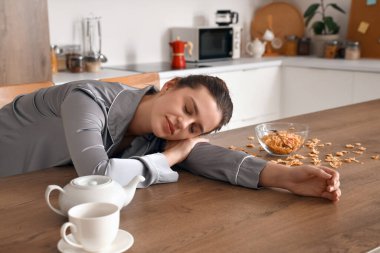 Genç bir kadın mutfakta kahvaltıda uyuyor.