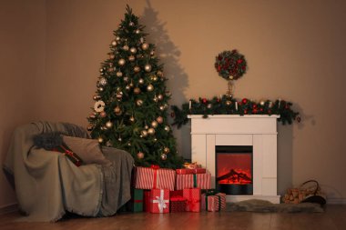 Karanlık oturma odasının içinde Noel ağacı, şömine ve koltuk var.