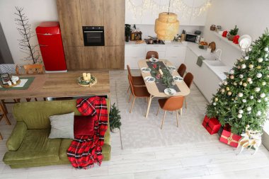 İçinde Noel ağacı, yeşil kanepe ve servis edilen yemek masası olan şenlikli bir mutfak.