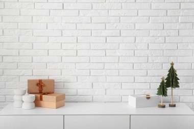 Beyaz tuğla duvarın yanında hediye kutuları ve Noel süslemeleri olan bir dolap.
