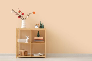 Bej duvarın yanında Noel dekoru olan ahşap raf ünitesi.