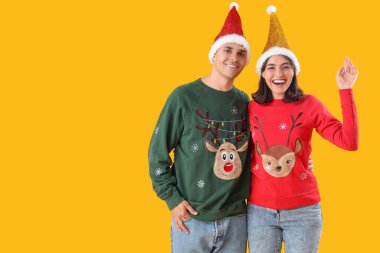 Sarı arka planda Noel kıyafetleri içinde mutlu genç bir çift