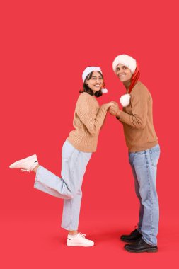 Kırmızı arka planda Noel Baba şapkalı mutlu çift