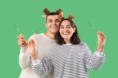 Mutlu genç çift Noel geyiği boynuzlarıyla yeşil arka planda maytaplar