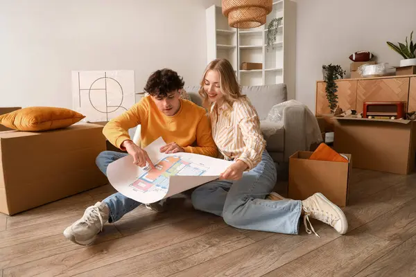 Young couple with house plan sitting in room on moving day