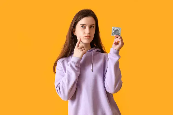 オレンジ色の背景にコンドームを持つ思慮深い若い女性 — ストック写真