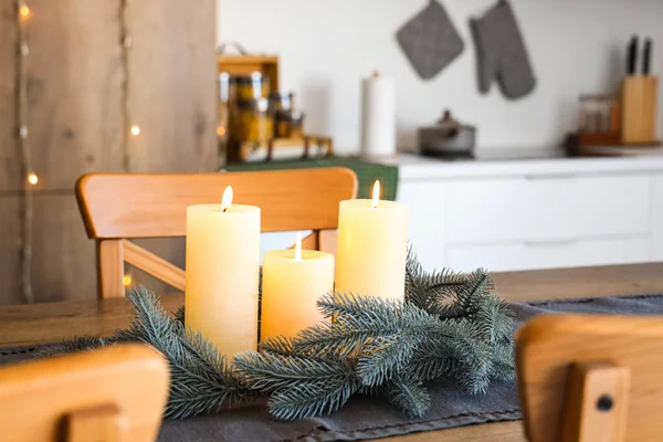 Burning candles and Christmas wreath on wooden table in kitchen, closeup