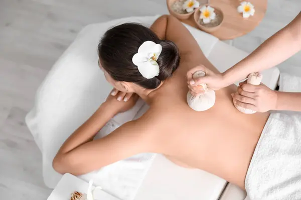 Young woman undergoing treatment with herbal bags in spa salon, top view