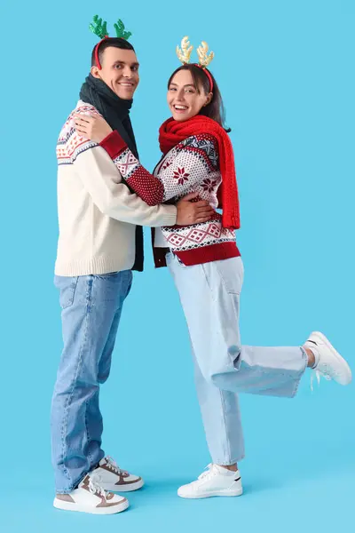 Счастливая Молодая Пара Рождественских Оленьих Рогах Теплых Шарфах Синем Фоне — стоковое фото