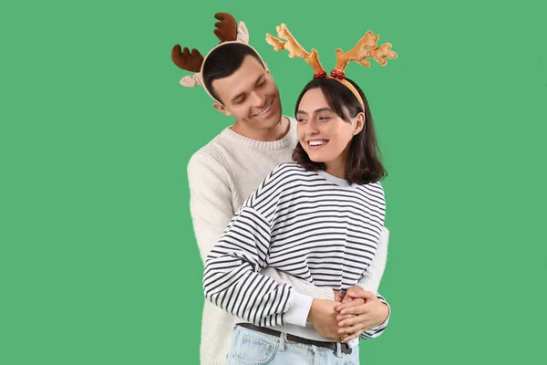Счастливая Молодая Пара Рождественских Оленьих Рогах Обнимающая Зеленом Фоне — стоковое фото