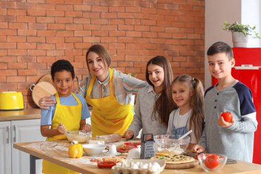 Mutfakta aşçılık kursu sırasında pizza hazırlayan bir grup küçük çocukla birlikte kadın şef.