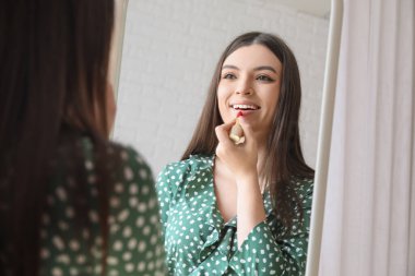 Evde aynanın önüne ruj süren genç bir kadın, yakın plan.