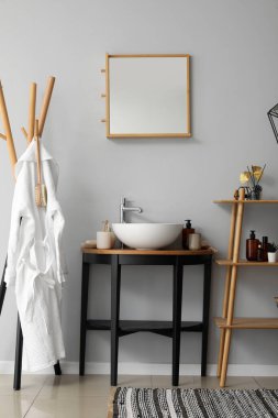 Banyonun içinde raf ünitesi, lavabo kasesi ve banyo aksesuarları var.