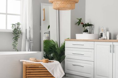 Beyaz tezgahların, aynaların ve küvetlerin üzerinde lavabo kasesi olan hafif bir banyo.